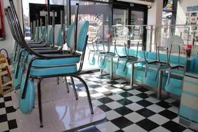 des tables et des chaises dans un snack-bar au sol à carreaux, devant une fenêtre