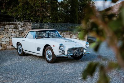 une voiture de collection blanche garée devant un mur de pierre
