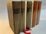 three books are lined up on a white surface with a red ribbon