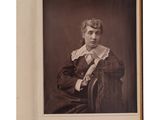 une vieille photo d'une femme assise sur une chaise, vêtue d'une chemise à col