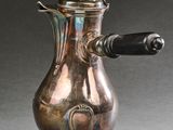 une cafetière en argent avec une poignée noire, posée sur un socle