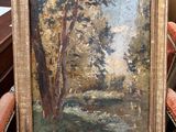 une peinture à l'huile représentant un paysage boisé, encadrée et posée sur une chaise