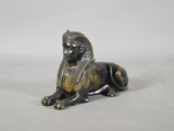 une statue en bronze représentant un sphinx assis sur une surface blanche