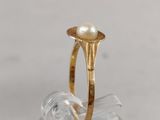 gold ring with a pearl in the middle of it on top of a clear piece of glass