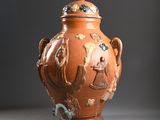 a brown vase with a lid that has animals and birds on it