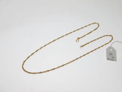 une chaîne en or à laquelle est accrochée une médaille, posée sur une surface blanche