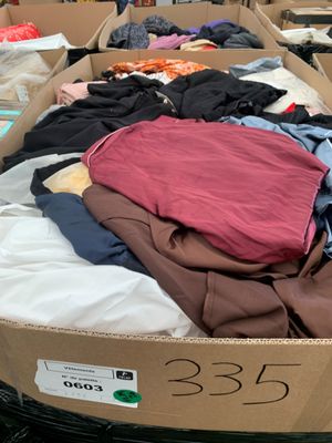 une boîte en carton remplie de nombreux vêtements, posée par terre