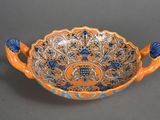 an orange and blue bowl with handles on a gray surface