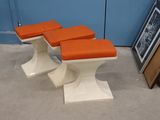 quatre tabourets avec des coussins orange, placés devant un mur bleu