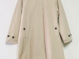 un trench-coat beige accroché à un mur blanc