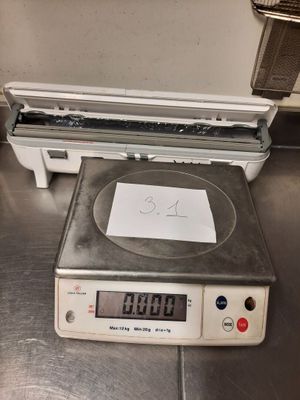 une balance posée par terre, sur laquelle se trouve une feuille de papier