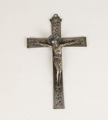 une croix en argent sur un mur blanc, surmontée d'un crucifix