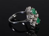 a close up of a diamond and emerald ring on a black surface