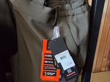 des pantalons suspendus à un portant dans un magasin de vêtements, avec leurs étiquettes encore attachées