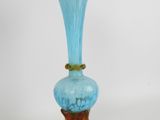 a blue glass vase with a wooden stand on a white surface