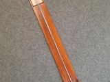 une grande horloge en bois munie d'une poignée en métal, posée sur un sol recouvert de moquette