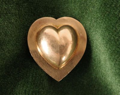 une broche en forme de cœur dorée posée sur un tissu vert