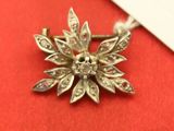 une petite broche en forme de fleur en argent posée sur un tissu rouge