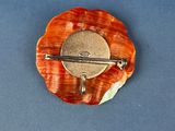 an orange flower brooch with a silver clasp on a blue surface