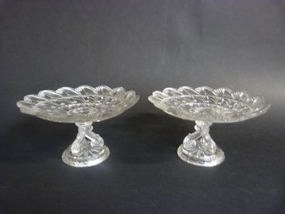 pair of clear glass footed dishes on pedestals on black background