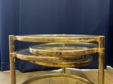 a round brass coffee table with glass top on a wooden floor