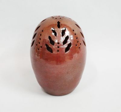 a red vase with holes in it on a white surface