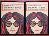 deux affiches représentant une femme aux cheveux roux et portant des lunettes, accrochées sur un mur rouge