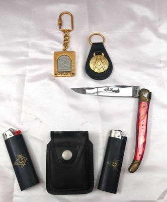 un couteau, un briquet, un étui à briquet et un porte-clés posés sur un drap blanc