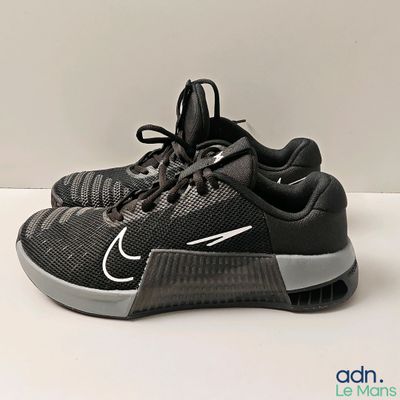 La chaussure est noire et comporte une bande blanche sur le côté.
