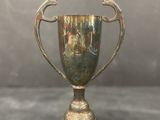 Coupe-trophée ancienne plaquée argent, posée sur un socle, sur fond gris