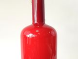 un vase rouge surmonté d'un couvercle doré, posé sur une surface blanche