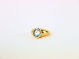 une bague en or sertie d'une topaze bleue repose sur une surface blanche
