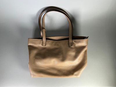 un sac fourre-tout en cuir beige accroché à un mur