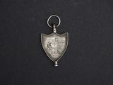 an old silver medal with a metal keychain on a black background