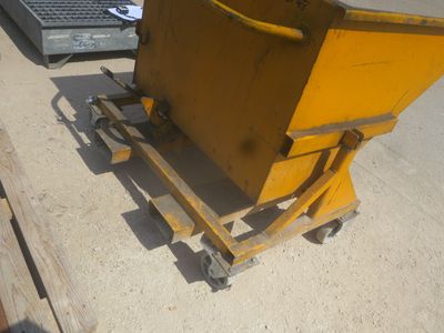 une benne jaune posée sur une palette à côté d'un tas de bois