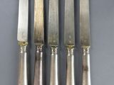 six silverplated knives and a knife on a gray surface