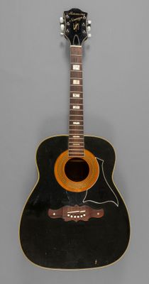 an old black acoustic guitar sitting on top of a gray surface