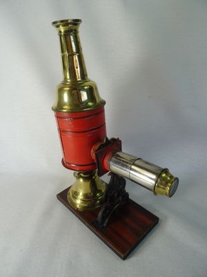 un microscope ancien en laiton et rouge, posé sur un socle en bois