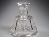 un flacon de parfum en verre à l'ancienne, avec un socle transparent posé sur une surface blanche