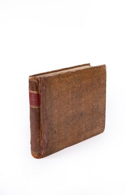 an old book with a red cover sitting on top of a white surface