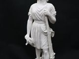 statue d'une femme tenant un bâton et portant un chapeau, sur fond noir