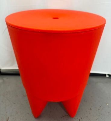 un tabouret orange posé par terre devant un mur blanc