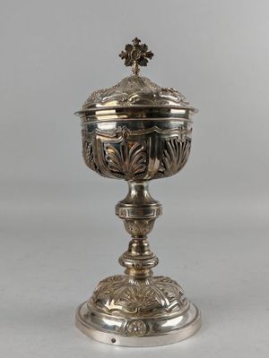 une urne ancienne en métal argenté, surmontée d'une croix