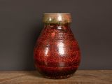 un vase rouge posé sur une table en bois, sur fond noir