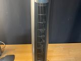 un ventilateur sur pied argenté posé sur une table en bois