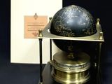 un globe noir et doré posé sur un socle, avec une boîte en arrière-plan