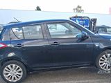 La petite voiture bleue est garée sur le parking, à côté d'autres voitures.