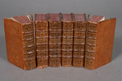 six old books are stacked on top of each other on a gray surface
