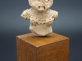 une figurine en céramique blanche représentant un homme coiffé d'un chapeau, posée sur un bloc de bois
