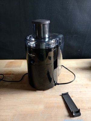 un mixeur noir posé sur une table en bois, à côté d'un téléphone portable